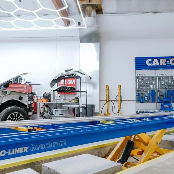 Vehicle undergoing collision repair beside professional frame-straightening equipment.