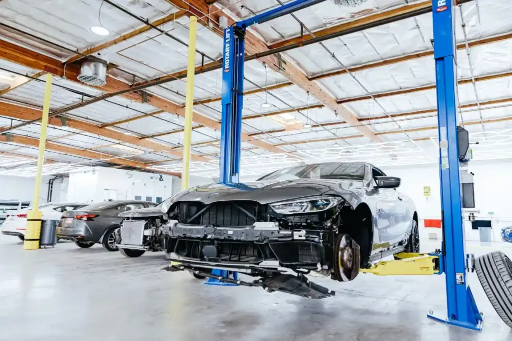 Damaged luxury car raised on a lift inside Network Auto Body, highlighting professional auto collision repair in Los Angeles.