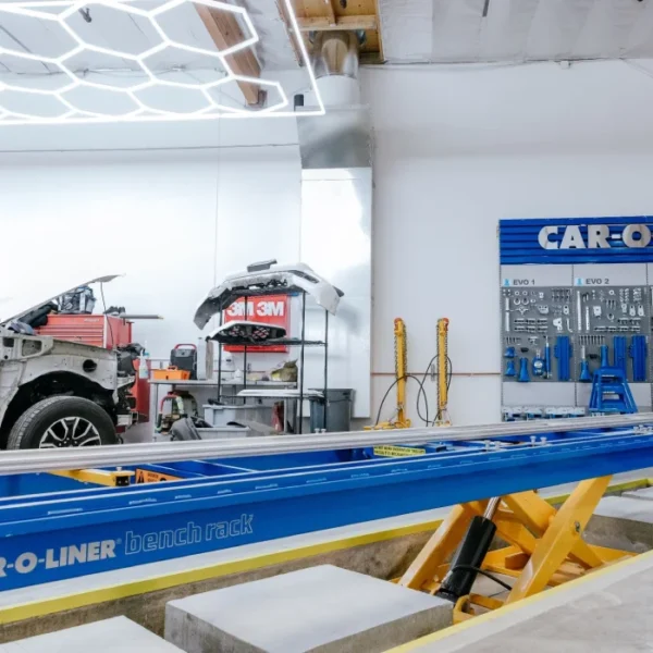 Vehicle undergoing collision repair beside professional frame-straightening equipment.